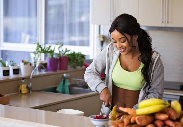 Smiling woman preparing fresh fruit in a sunlit kitchen, embodying a healthy lifestyle.